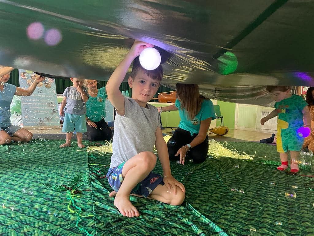 A child holding a light-up ball under the class parachute