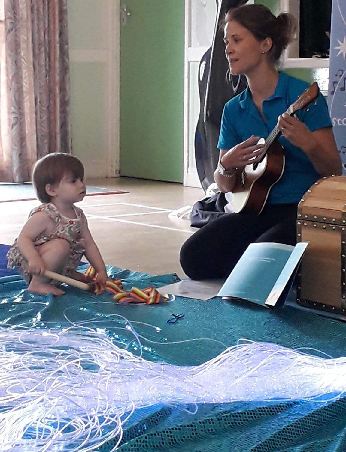 A StoryBox leader playing guitar for babies