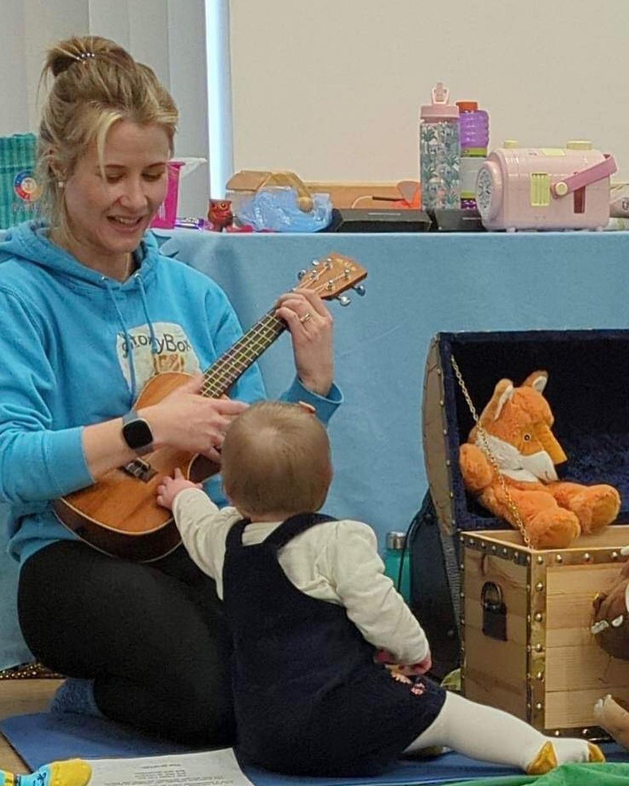 A StoryBox leader playing ukulele with a baby